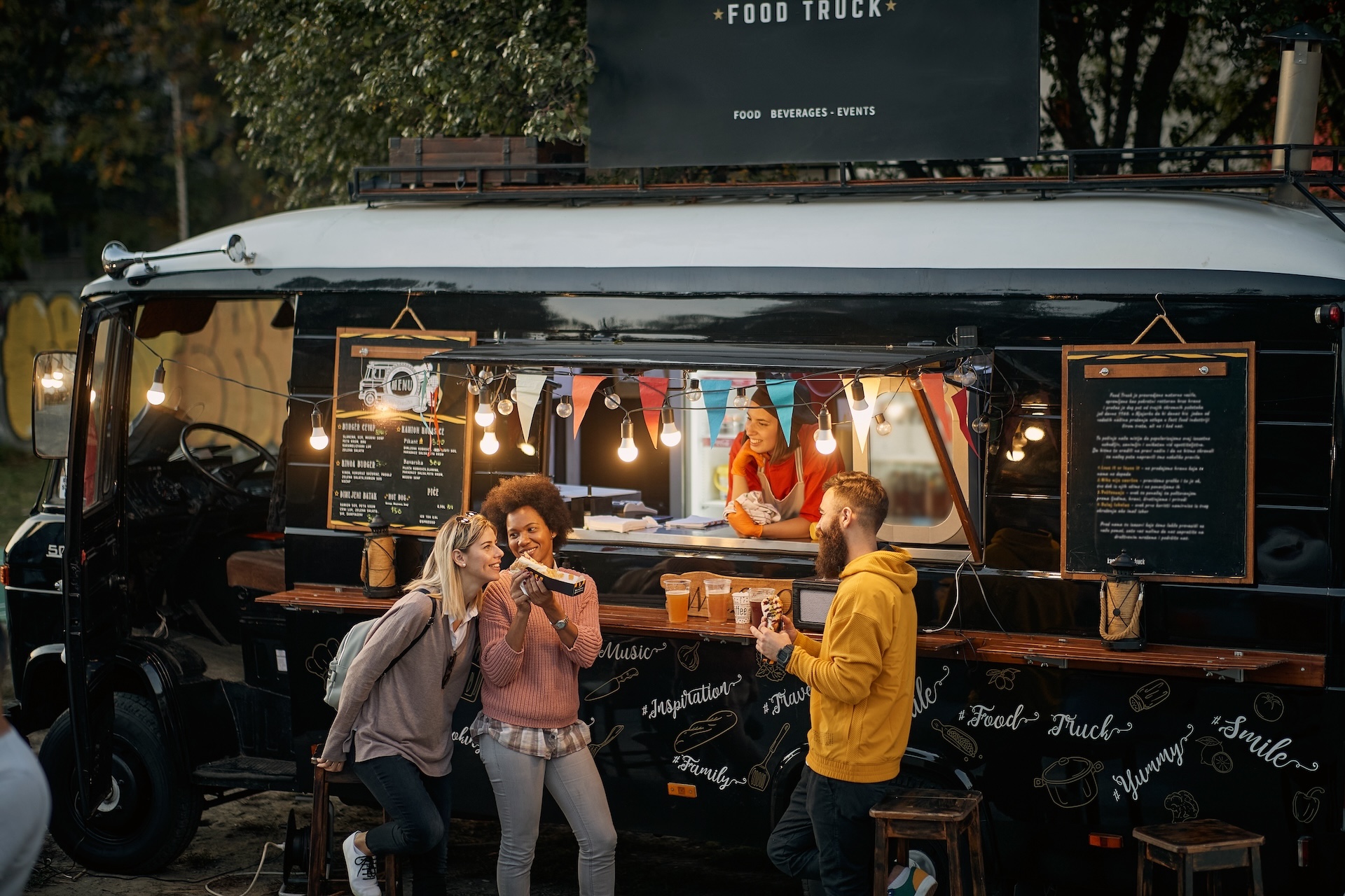 Group of people socializing while eating outdoor in front of modified truck for fast food